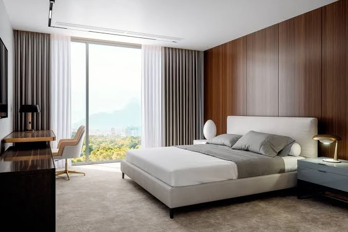 Modern luxury hotel bedroom with a king-size bed, white linens, gray pillows, wood-paneled walls, and large windows.